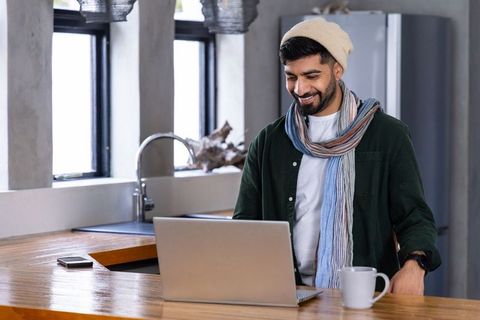 Young man working on laptop at modern kitchen island with coffee and smartphone