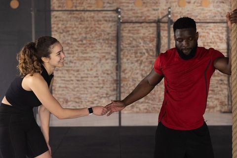 Smiling woman reaching smartwatch while male training partner holding rope in urban gym