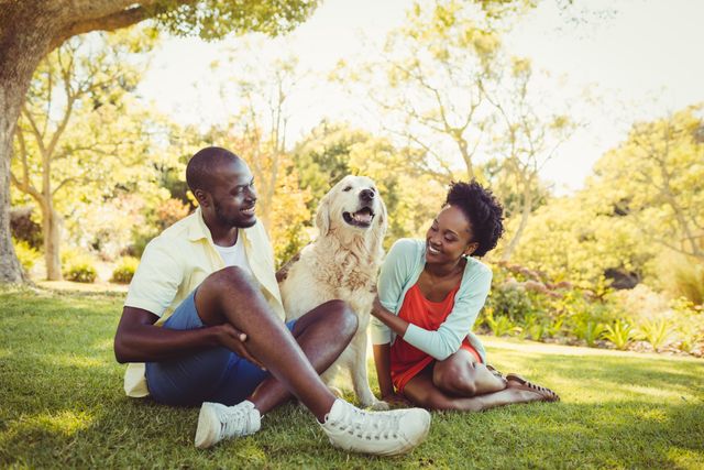 Couple sitting on grass with their dog in a park, enjoying a sunny day. Ideal for themes of companionship, outdoor activities, pet ownership, and leisure time. Perfect for advertisements, blogs, and social media posts about pets, relationships, and outdoor fun.