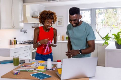 African american couple planning healthy meals in bright kitchen with laptop and tape measure