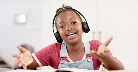 Joyful Girl Singing with Headphones and Book Indoors