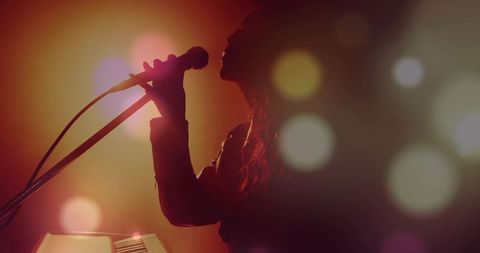 Silhouette vocalist singing into microphone on warm backlit stage with dramatic bokeh