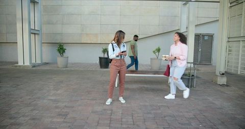 Young women chatting with coffee and smartphone at urban courtyard casual streetwear lifestyle