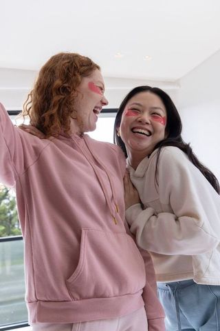 Laughing multicultural friends leaning in wearing hoodies with pink hydrogel eye patches