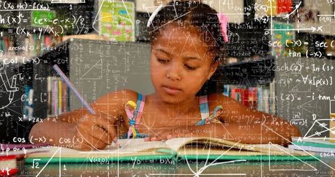 Young girl studying math in library writing in notebook with pencil and stacked textbooks