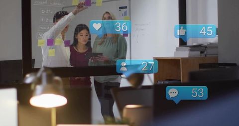 Team collaborating around glass wall with sticky notes and tablet for creative planning
