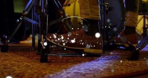 Drummer pressing bass drum pedal on patterned rug with amber and blue stage lighting