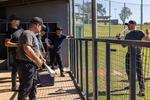 Mature teammates gathering in baseball dugout holding metal bats planning practice