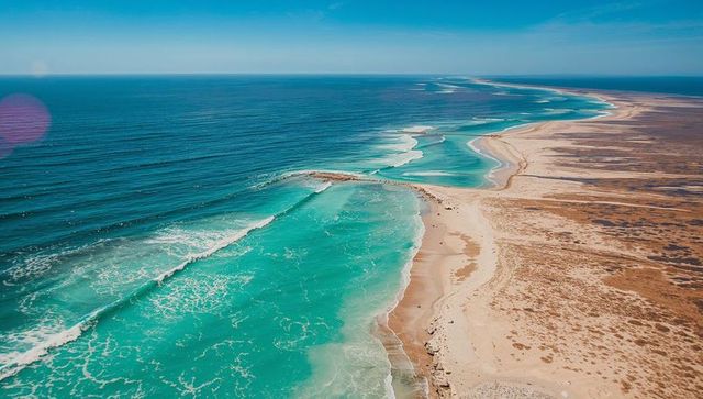 Turquoise waves meeting arid shoreline along serpentine sandbar