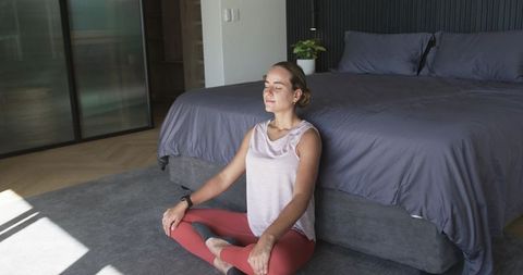 Woman meditating cross-legged in minimalist sunlit bedroom wearing smartwatch