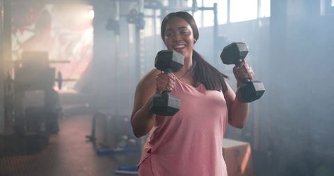 African american woman lifting hex dumbbells in gym smiling with confident, joyful workout