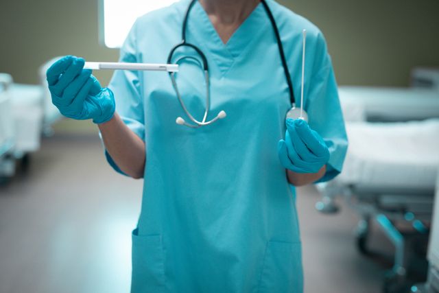 Midsection of a Caucasian female doctor wearing blue scrubs and gloves, holding a pipette for COVID-19 testing in a hospital. Ideal for use in articles, blogs, and educational materials related to healthcare, COVID-19 testing, medical professionals, and pandemic response.