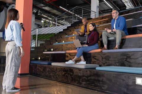 Asian presenter addressing diverse coworkers on tiered seating in modern amphitheater