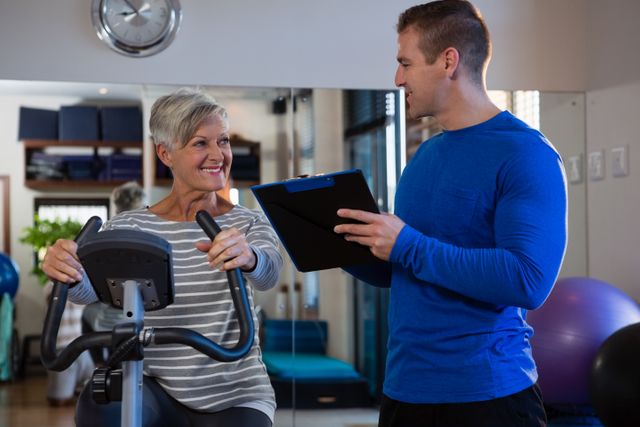 Physiotherapist interacting with senior woman while exercising on exercise bike - Download Free Stock Photos Pikwizard.com