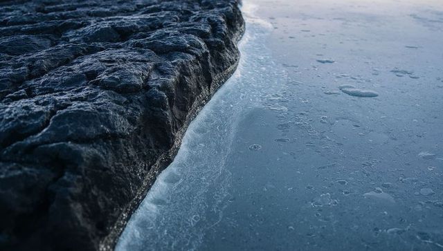 Dark rock meeting smooth lake ice with frost rim and bubble texture