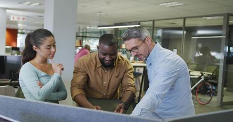 Team collaborating at workstation in modern open office leaning over computer screen