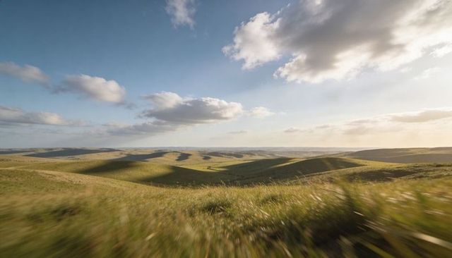 Rolling grassland panorama stretching under dramatic cloudscape