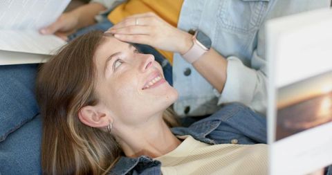 Reclining female couple sharing tender moment on couch, woman resting head on partner lap