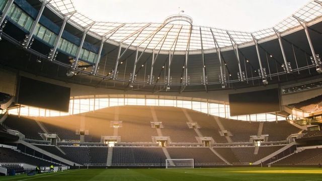 Sunlight streaming through modern football stadium roof revealing empty stands and goal