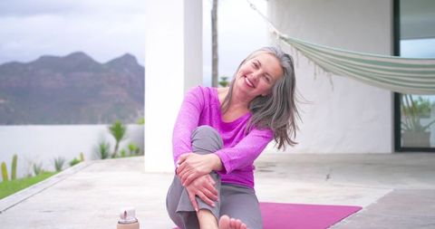 Mature woman smiling and stretching on terrace yoga mat, serene outdoor wellness routine