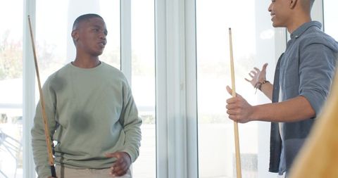 Young men playing pool in sunlit living room near glass doors