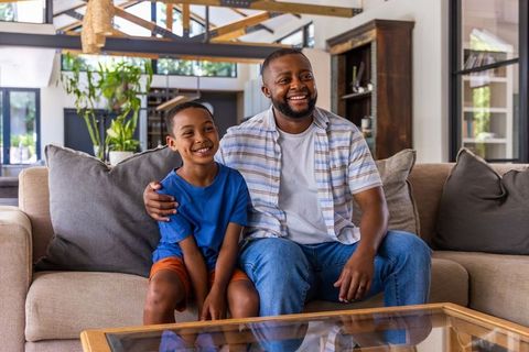 Smiling african american father and son sitting on sofa in modern open-plan living room