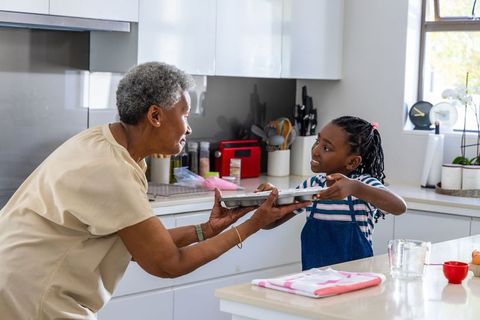 African american grandmother and granddaughter sharing baking tray in modern bright kitchen
