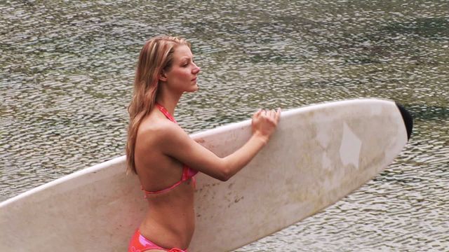 Woman in swimsuit holding surfboard at the ocean's edge, highlighting adventure and active beach lifestyle. Suitable for content on travel, surfing sports, and summer adventures.