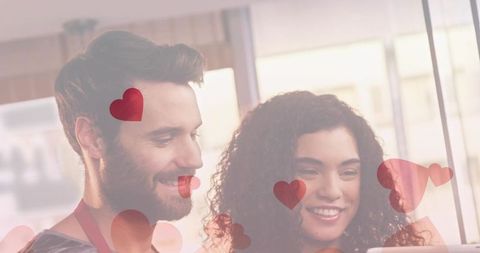 Couple smiling and leaning over tablet with heart overlays in cozy kitchen light