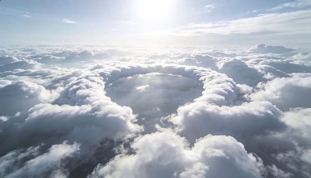 Annular cloud crater forming over sunlit high-altitude sky with radiant sunbeams