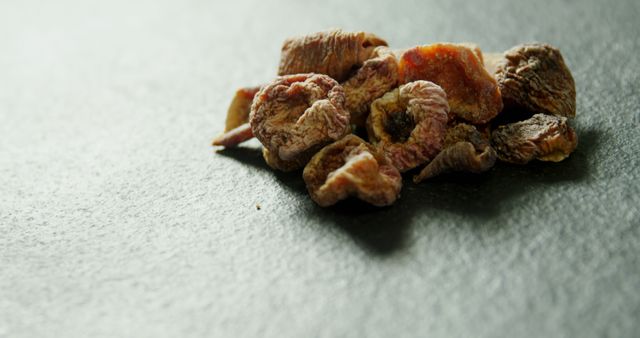 Dried figs are arranged on a textured gray surface, providing a natural and healthy snack option. Their wrinkled appearance and rich golden-brown hues indicate the natural drying process that concentrates their sweetness.