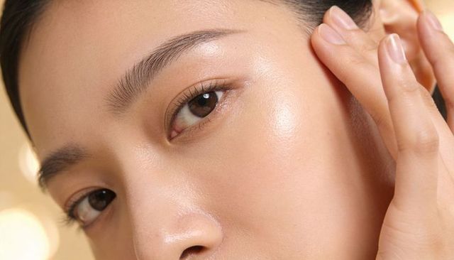 Dewy glowing skin touching cheek with manicured hand, radiant skincare close-up