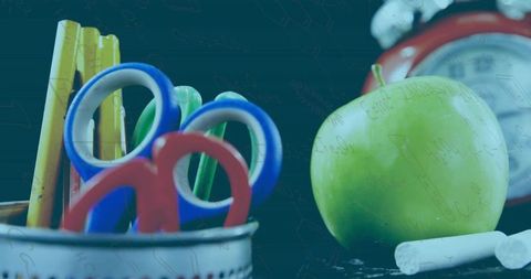 Colorful school supplies on desk with apple and clock