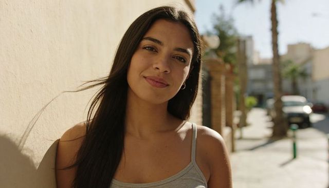 Smiling young woman leaning against beige wall on sunlit urban street portrait