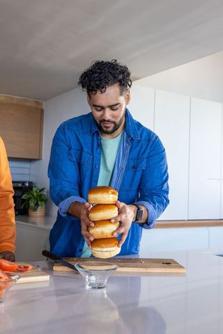 Man holding stack of glossy burger buns while preparing meal on modern kitchen counter