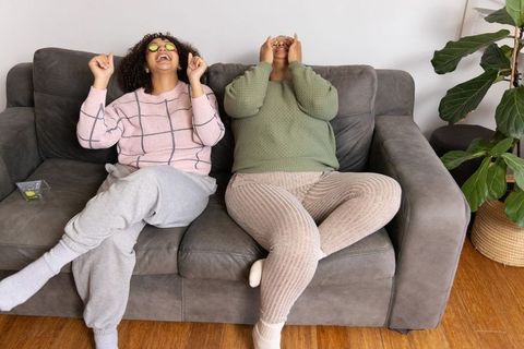 African american friends laughing and relaxing on sofa applying cucumber eye patches