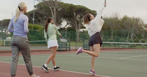 Women practicing serves on outdoor tennis court in casual athleticwear, training session