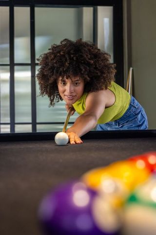 African american woman wearing lime top lining up pool shot on black-felt table in game room