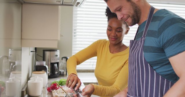 Image of happy diverse couple preparing meal in kitchen. Love, relationship and spending quality time together at home.