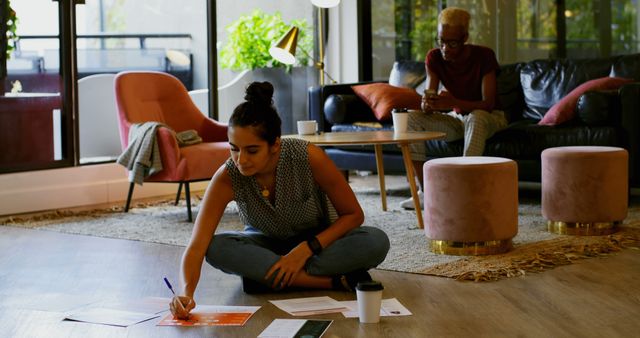 Young Woman Working on Floor in Home Office with Older Roommate in Background - Download Free Stock Images Pikwizard.com