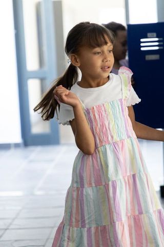 Girl wearing pastel striped dress walking through bright school hallway, candid moment