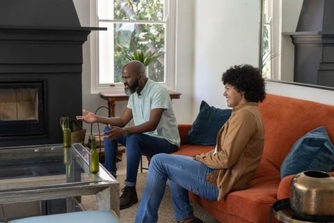 Diverse friends chatting on orange sofa in cozy living room with fireplace and daylight