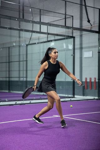 Indian woman lunging for padel shot on purple indoor court in black sportswear