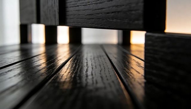 Glossy dark-stained oak floor planks reflecting warm backlight beneath low modern bench, close-up