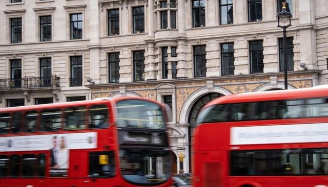 Passing red double-deck buses sliding past historic stone facade on urban london street