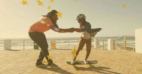 Teaching child to skateboard on sunlit coastal boardwalk, holding hands for balance, family bonding