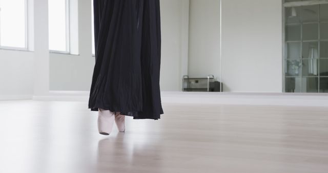 Low section of female ballet dancer in long black dress practicing at dance studio, copy space. Dance, ballet, discipline, practice and training, unaltered.