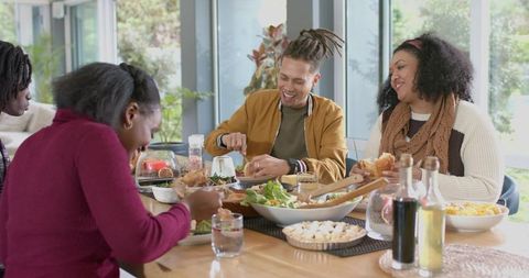 Multiracial friends sharing salad and laughing at sunlit wooden dining table