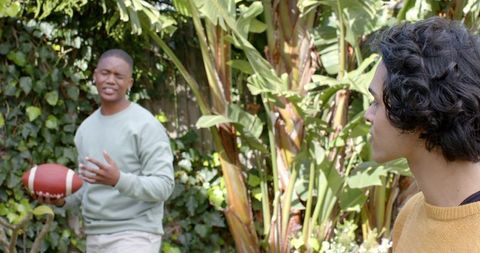 Multicultural friends playing casual backyard football in sunlit tropical garden