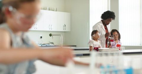 African american teacher guiding girls through pipetting experiment in school science lab